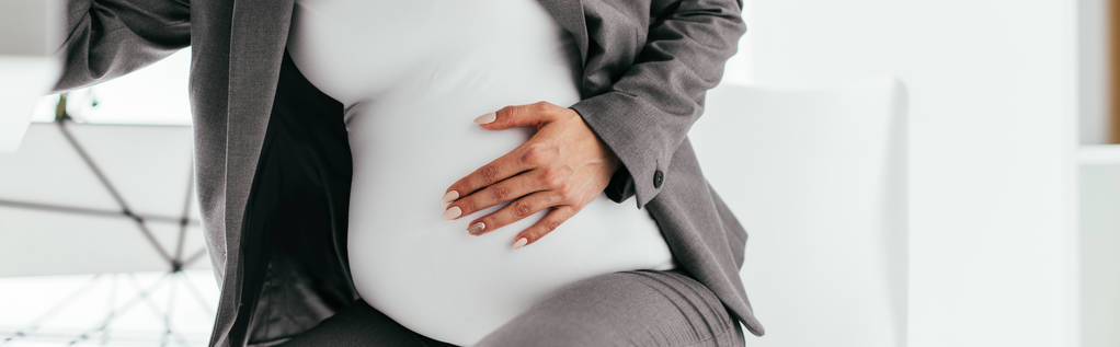 plano panorámico de la mujer embarazada sosteniendo su vientre y sentado detrás de la mesa
 - Foto, Imagen