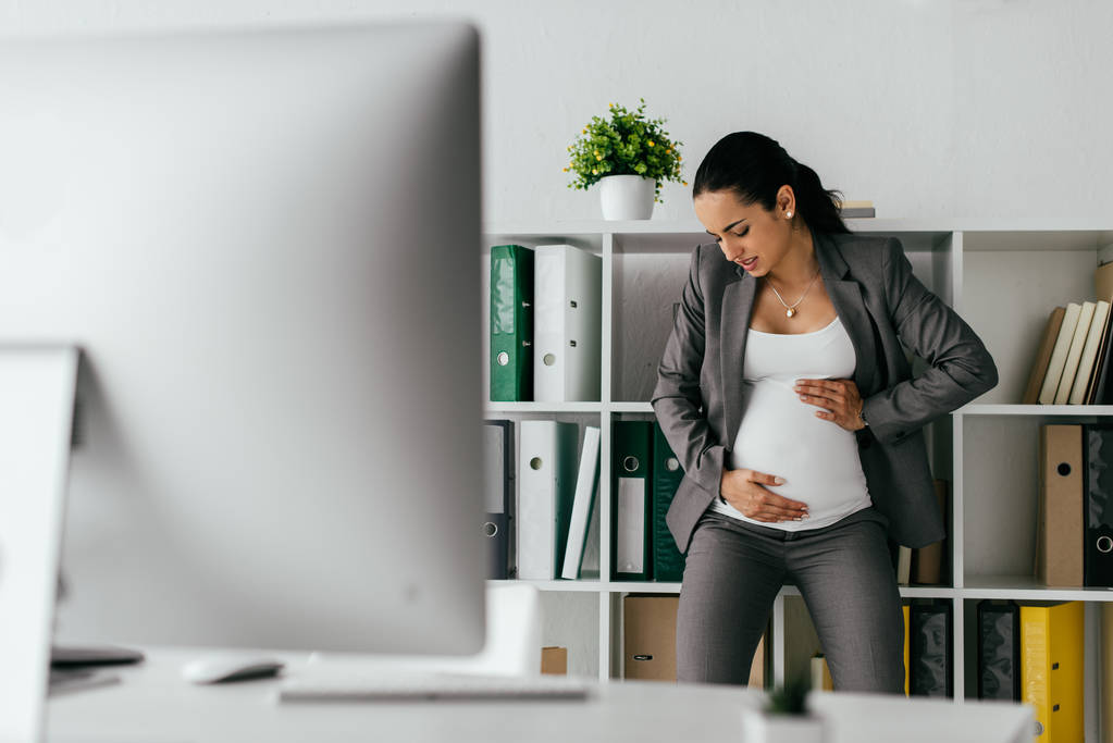 mujer embarazada tensa de pie cerca de la estantería y la celebración del vientre
  - Foto, imagen