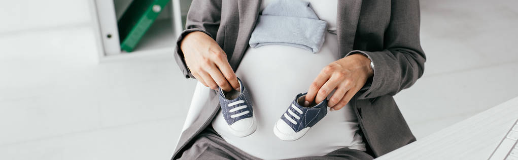 panoramische foto van zwangere vrouw die kleine gumshoes vasthoudt - Foto, afbeelding