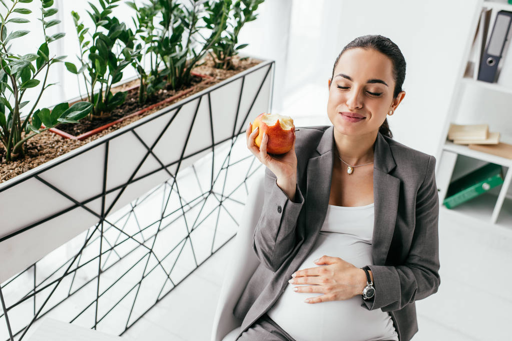 těhotná žena, která při sezení v kanceláři jedla jablko - Fotografie, Obrázek