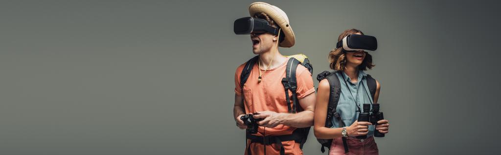 панорамний знімок двох молодих туристів з використанням гарнітури віртуальної реальності на сірому фоні
 - Фото, зображення