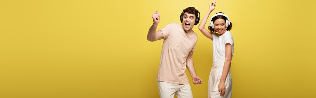 πανοραμική φωτογραφία ενθουσιασμένο άντρα και γυναίκα που χορεύει ακούγοντας μουσική στα ακουστικά σε κίτρινο φόντο - Φωτογραφία, εικόνα