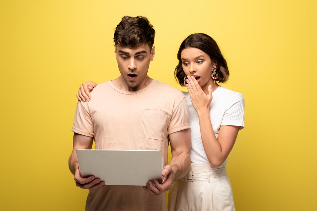 scioccato giovane ragazza in piedi vicino fidanzato sorpreso utilizzando computer portatile su sfondo giallo
 - Foto, immagini