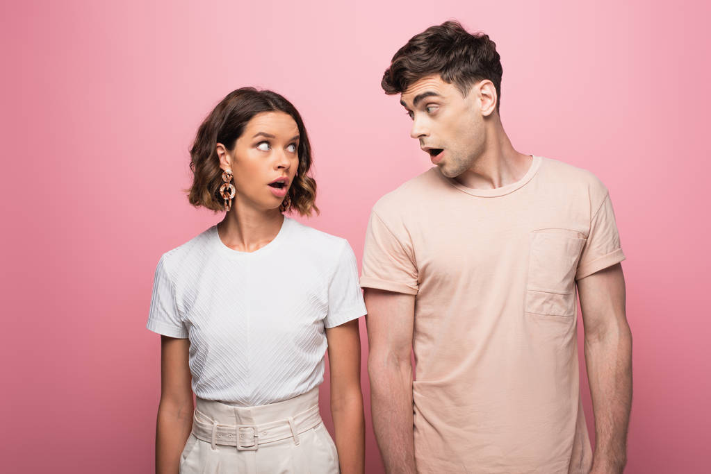 young couple quarreling while looking at each other on pink background - Photo, Image