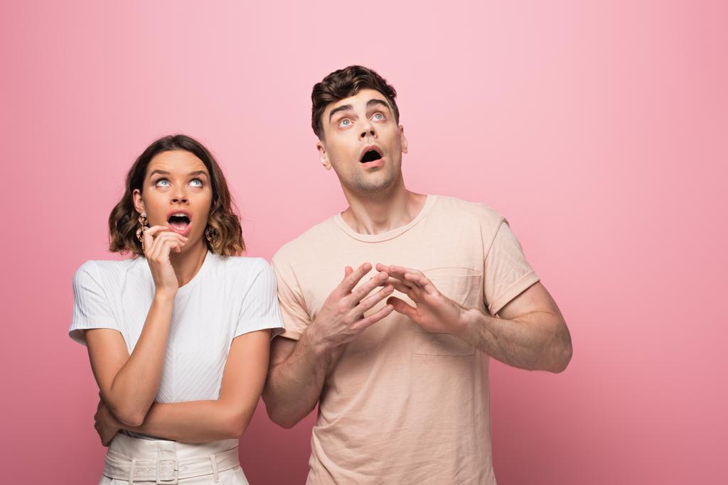 surprised man and woman gesturing while looking up on pink background - Photo, Image