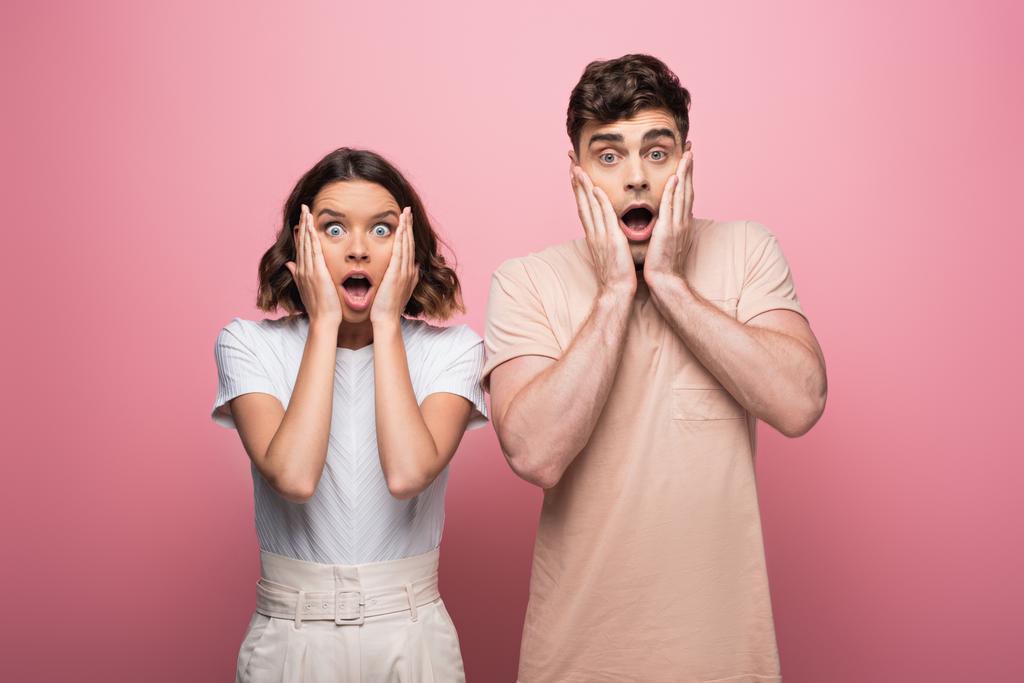 shocked man and woman holding hands near face while looking at camera on pink background - Photo, Image
