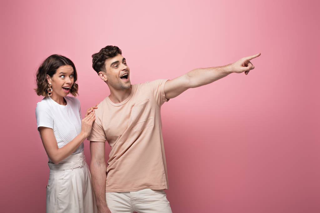 excited man pointing with finger near surprised woman on pink background - Photo, Image