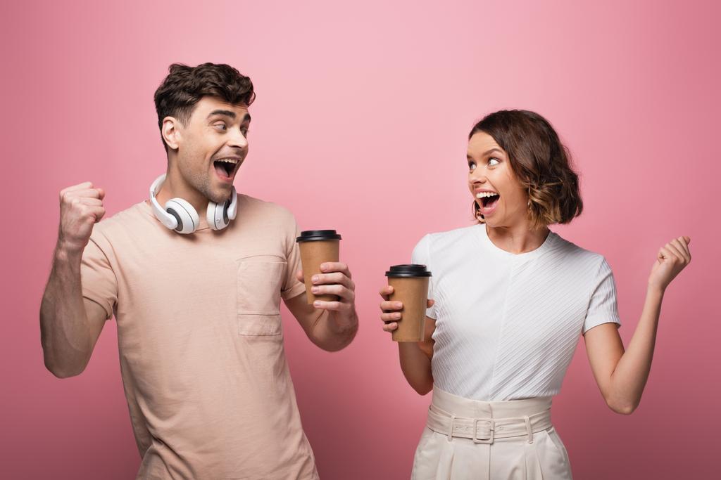 boldog ember és nő mutatja igen gesztusok, miközben papír csészék és nézi egymást, rózsaszín háttér - Fotó, kép