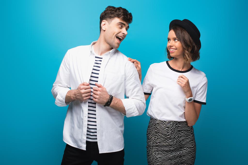 vrolijke, trendy man en vrouw die op een blauwe achtergrond naar elkaar kijken - Foto, afbeelding