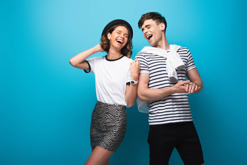  junges, fröhliches Paar lacht gemeinsam auf blauem Hintergrund - Foto, Bild