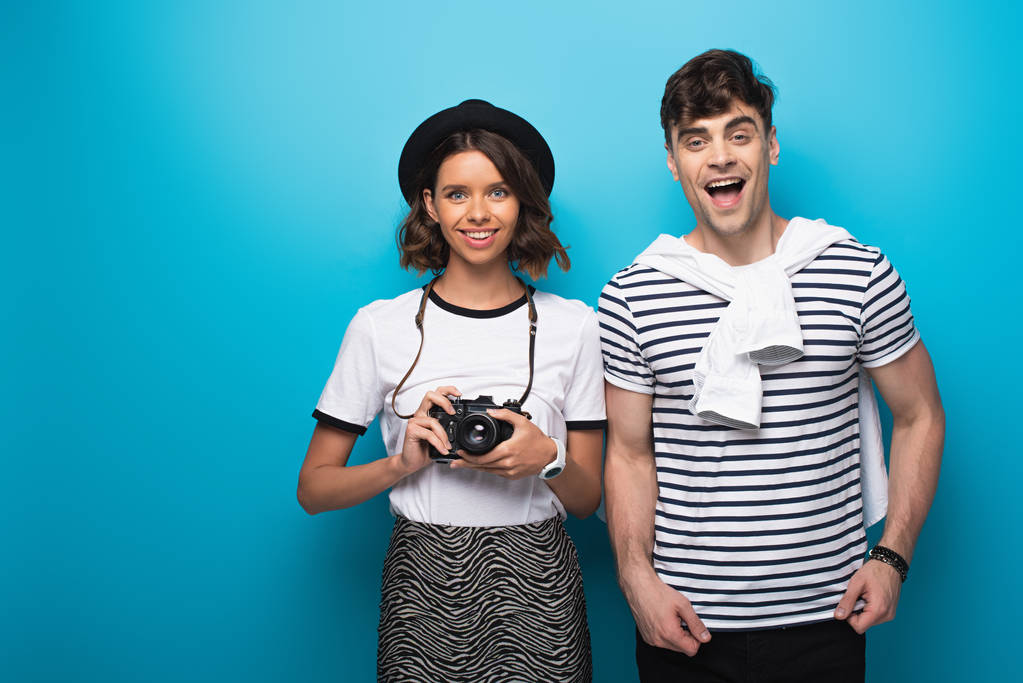 Lächelndes Mädchen mit Digitalkamera und fröhlicher Mann, der auf blauem Hintergrund in die Kamera blickt - Foto, Bild