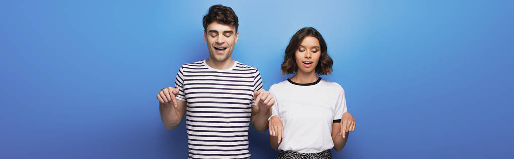 plan panoramique de l'homme et de la femme regardant vers le bas et pointant avec les doigts sur fond bleu
 - Photo, image