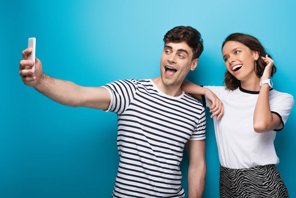 vrolijke man neemt selfie met mooi jong meisje op blauwe achtergrond - Foto, afbeelding
