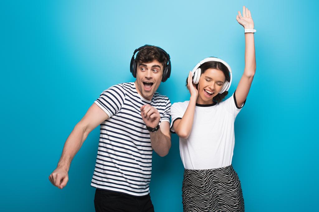 щасливий чоловік і жінка танцюють під час прослуховування музики в навушниках на синьому фоні
 - Фото, зображення