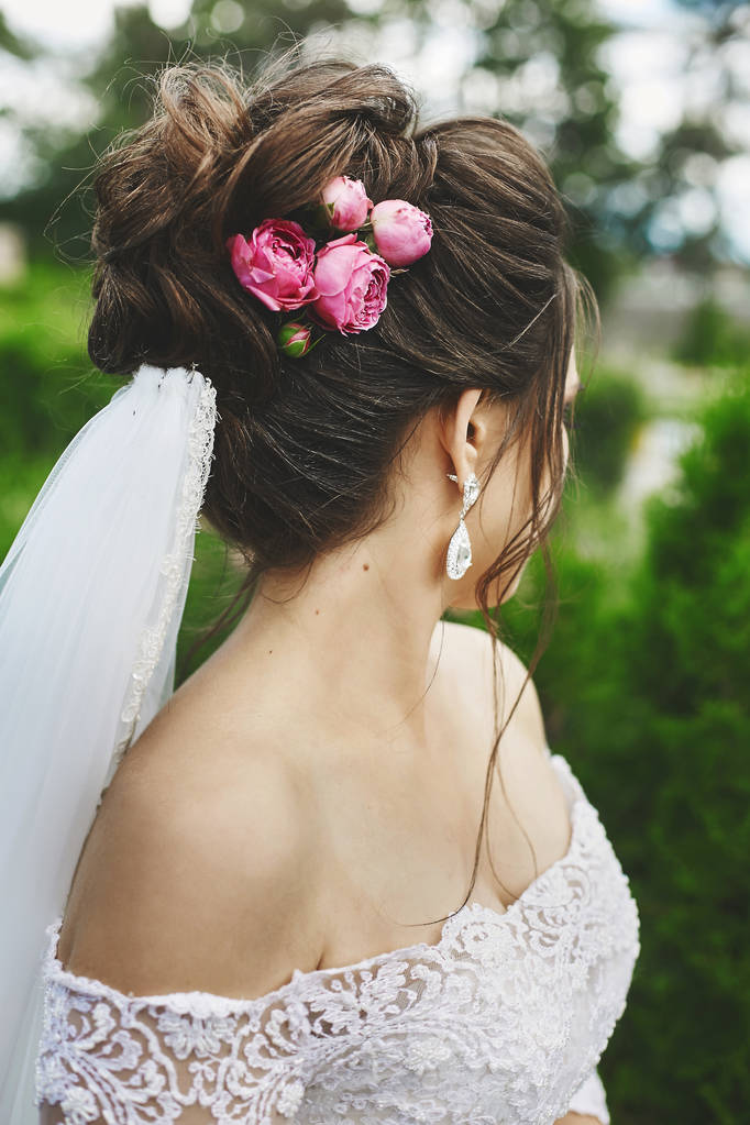 Όμορφο συν μέγεθος γυναίκα μοντέλο με κομψό γάμο χτένισμα διακοσμημένο με τριαντάφυλλα λουλούδια σε ένα μοντέρνο νυφικό και σε ένα πέπλο που θέτουν σε εξωτερικούς χώρους - Φωτογραφία, εικόνα