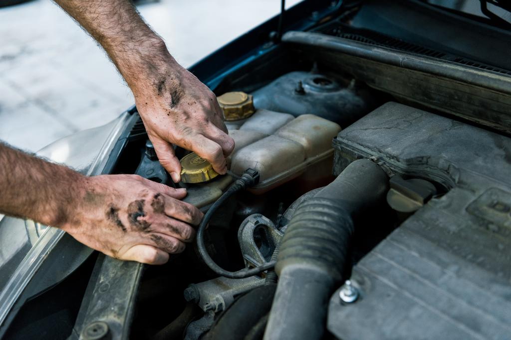 abgeschnittene Ansicht von Automechaniker mit Schlamm auf Händen beim Ölwechsel  - Foto, Bild