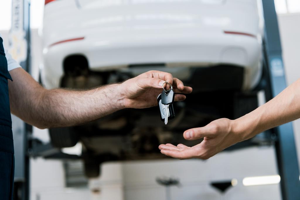 bijgesneden weergave van automonteur het geven van sleutel aan de mens in de garage  - Foto, afbeelding
