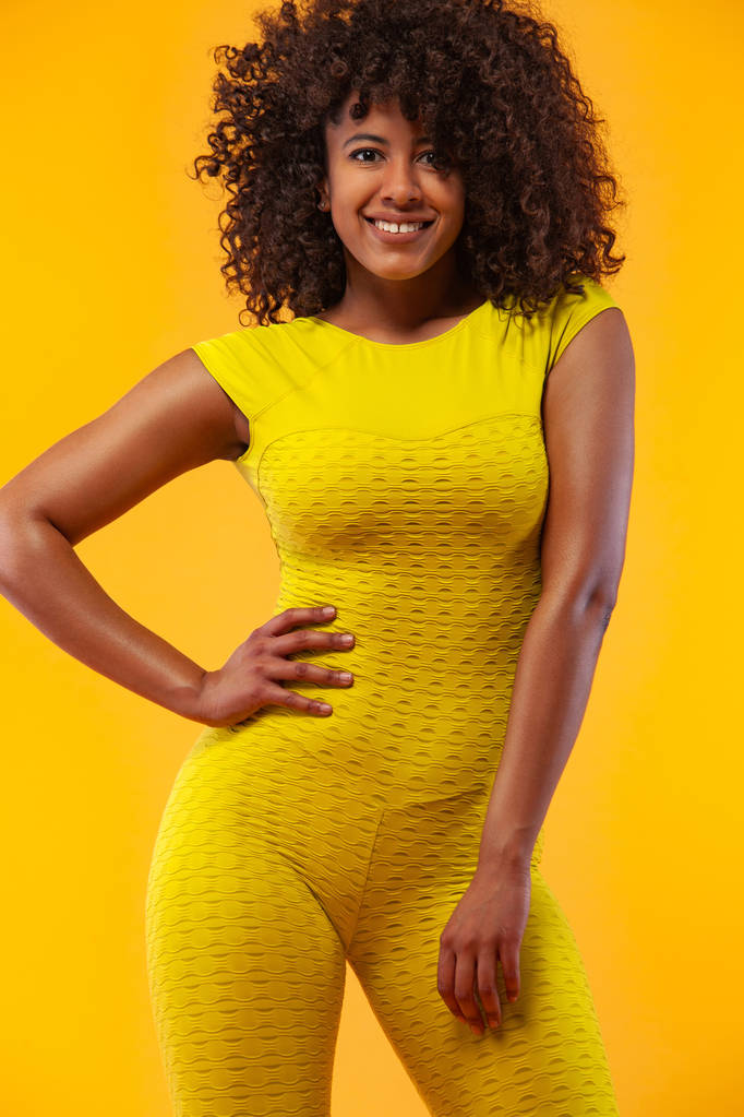 Lachende sterke atletische vrouw met zwarte huid en krullend haar, doen oefening op gele achtergrond dragen sportkleding. Fitness en sportieve motivatie. - Foto, afbeelding