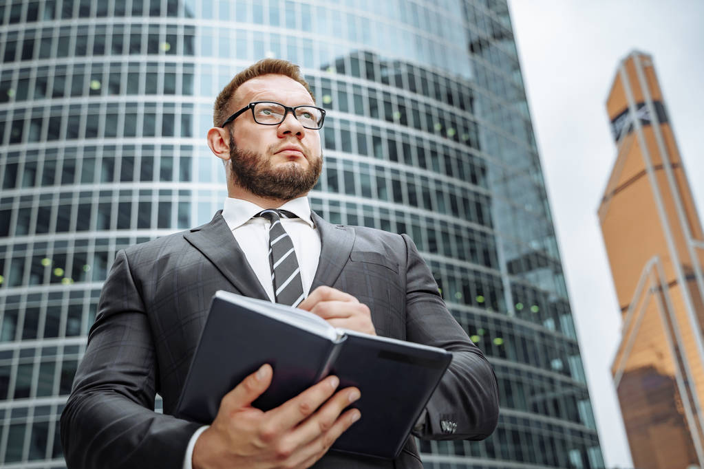 Ritratto di un uomo d'affari di successo in giacca e cravatta e occhiali con un taccuino in mano sullo sfondo del business center
 - Foto, immagini