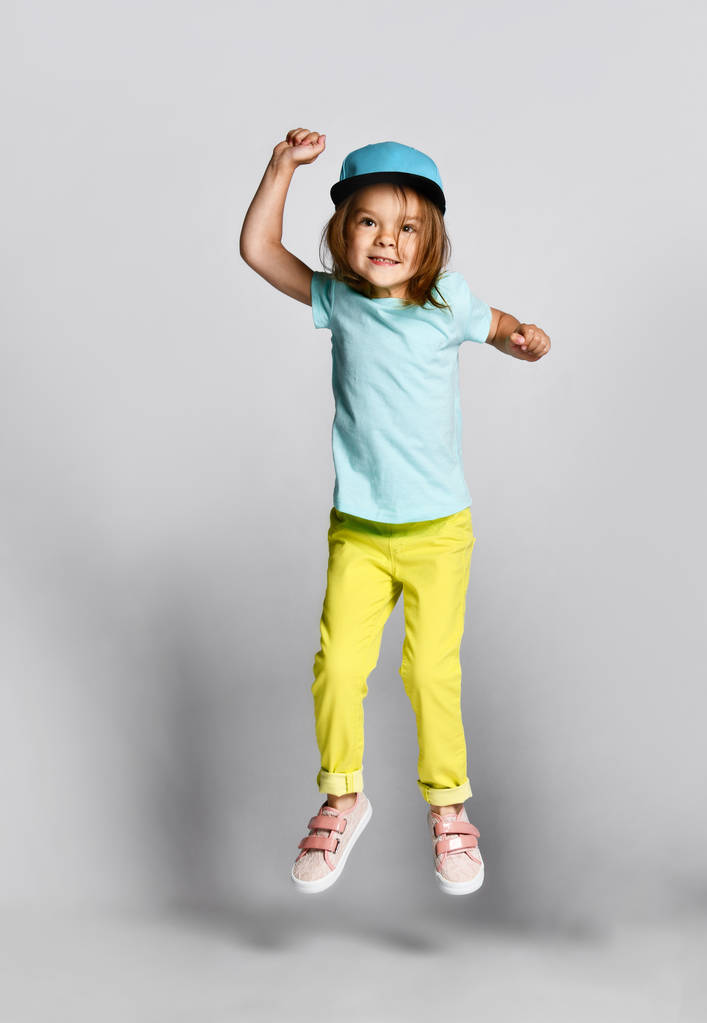 Excited joyful little girl in fashion outfits jumping over light background - Fotoğraf, Görsel