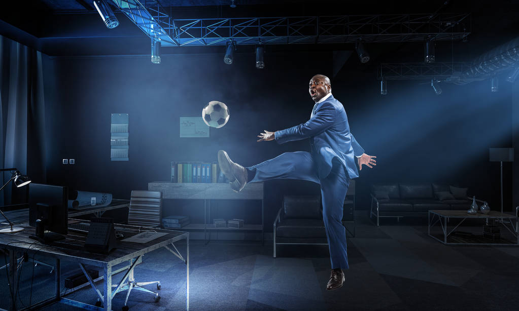 Musta liikemies puvussa pelaa jalkapalloa
 - Valokuva, kuva