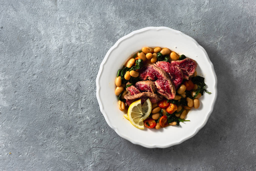 Biftek, beyaz fasulye, ıspanak ve domates ile akşam yemeği tabağı kopya alanı ile üst görünümü - Fotoğraf, Görsel
