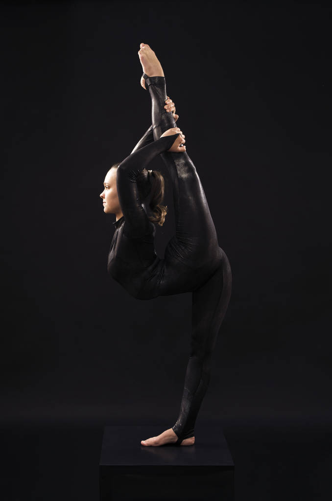 Egy bájos lány tornász, egy fekete öltönyt, részt akrobatika fényében a Contra. - Fotó, kép