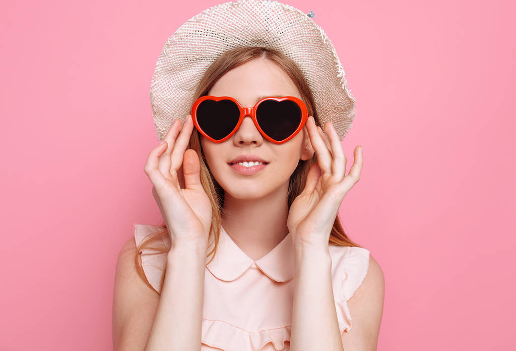 Portret van een vrolijk meisje in een zomer hoed en hartvormige zonnebrillen wachten op een vakantie - Foto, afbeelding