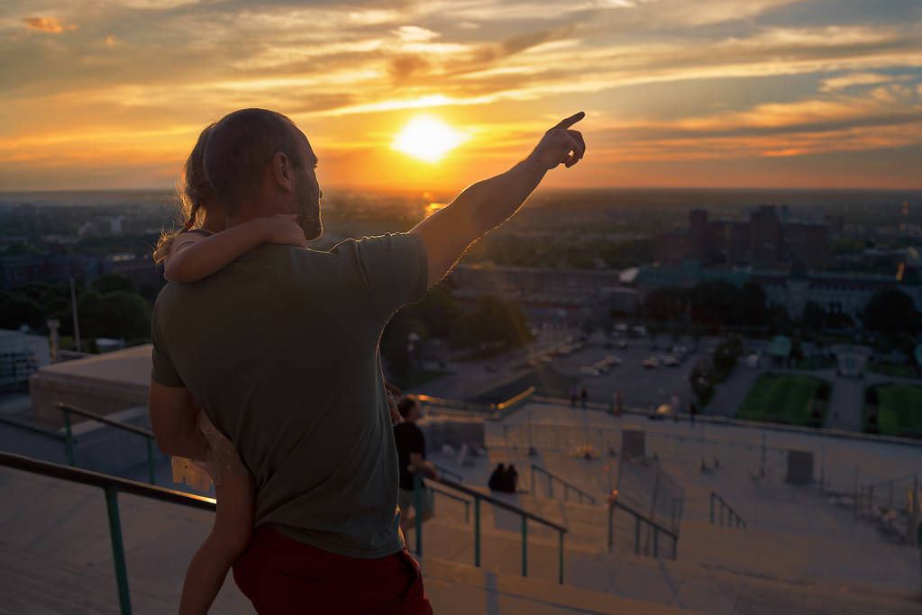 Hombre con una niña en sus brazos, mirando el atardecer sobre Montreal en una noche de verano. Cuidado de los padres, padre viaja con su hija. Viajes de Canadá
 - Foto, imagen
