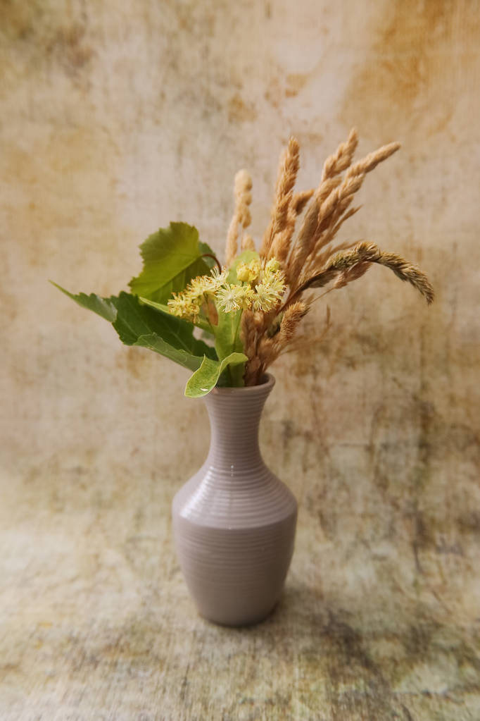 Biały wazon z bukietem pachnących żółtych kwiatów i liści lipy i suszonych jeży trawiastych. - Zdjęcie, obraz