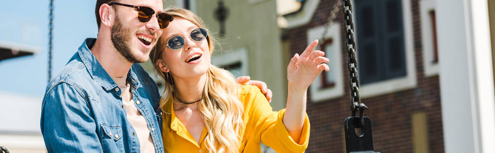 plano panorámico de mujer alegre en gafas de sol apuntando con el dedo cerca de hombre guapo
  - Foto, imagen