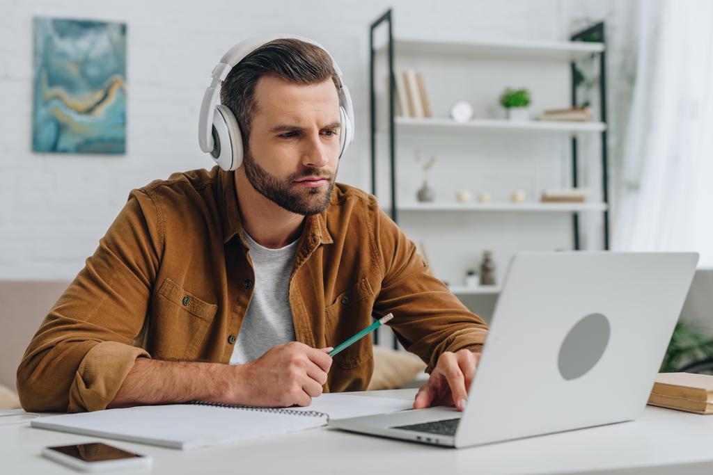  hombre guapo escuchando música, sosteniendo el lápiz y usando el ordenador portátil
  - Foto, imagen