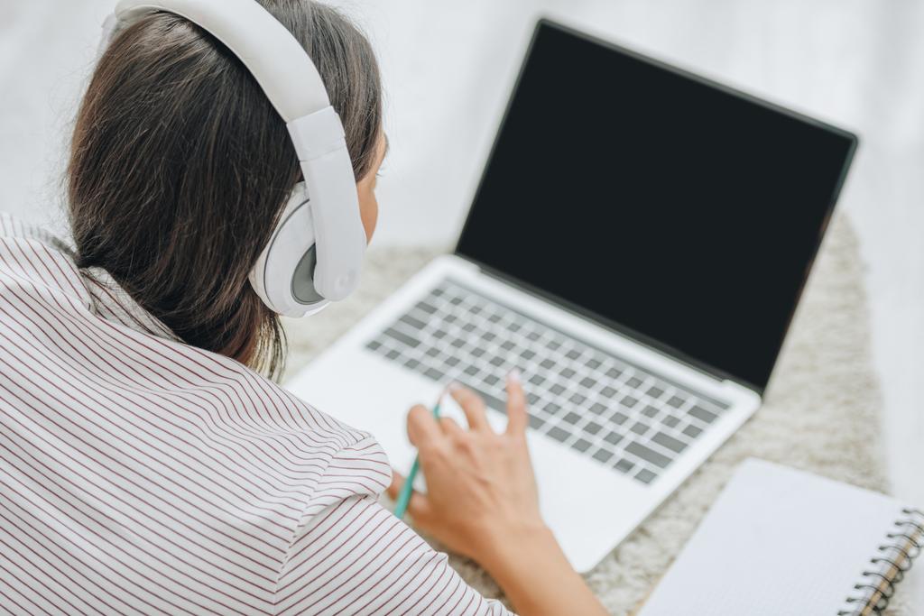 visão traseira da mulher com fones de ouvido usando laptop e segurando lápis
  - Foto, Imagem
