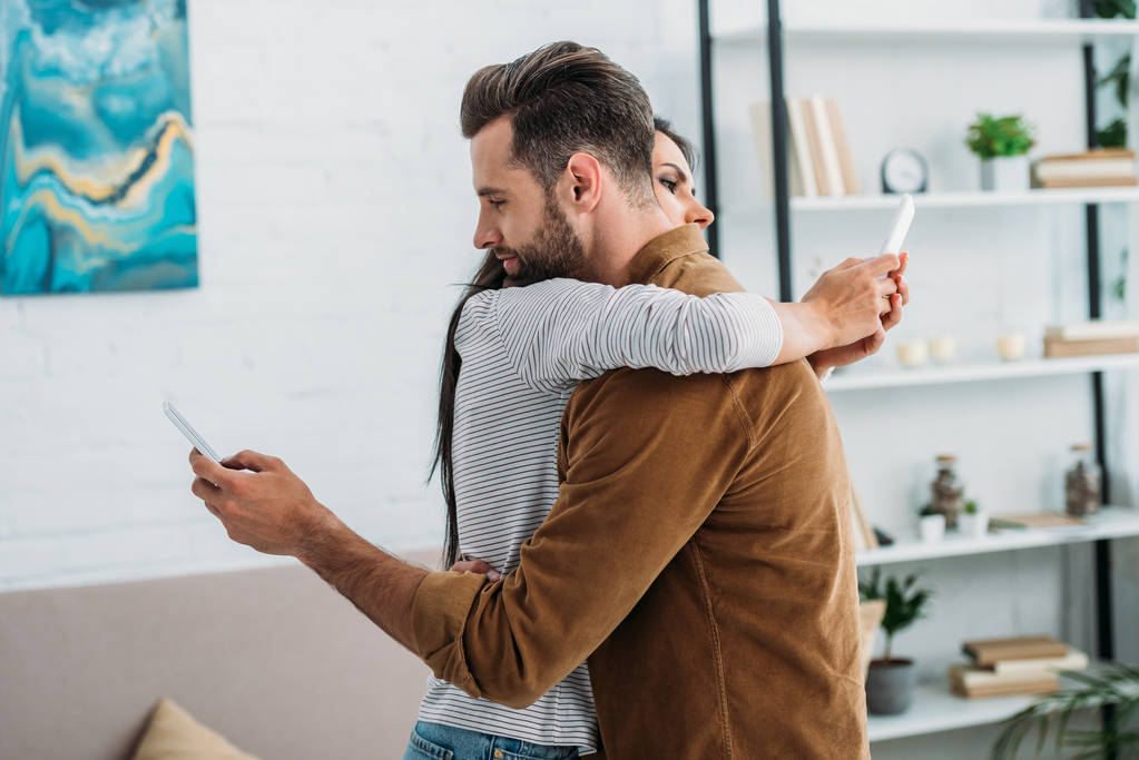 knappe man knuffelen met aantrekkelijke vrouw en het gebruik van smartphones  - Foto, afbeelding