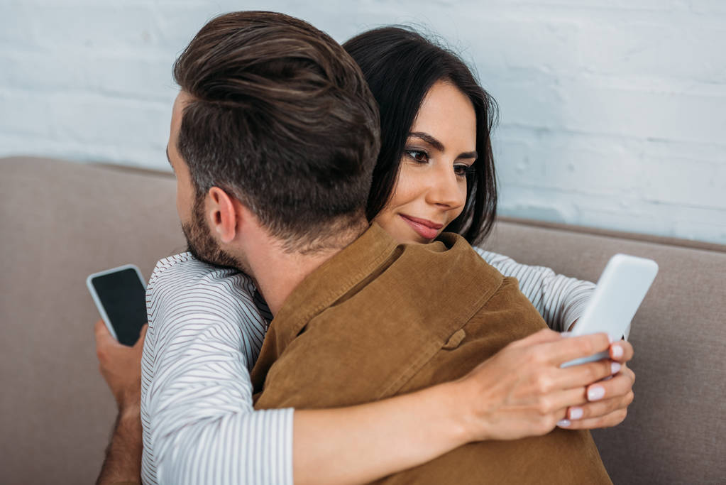 man and attractive, brunette woman hugging and using smartphones  - Photo, Image