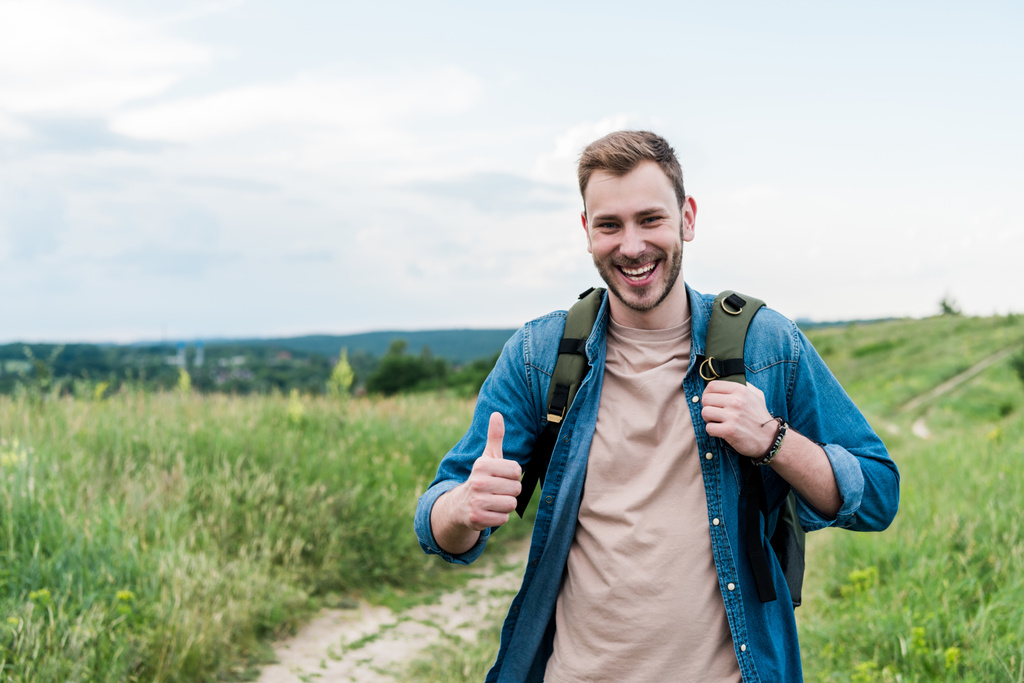 boldog fiatal férfi mutatja hüvelykujját fel állva hátizsák  - Fotó, kép