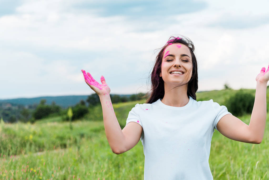 目を閉じてピンクの粉を手にして立っている幸せな若い女性  - 写真・画像