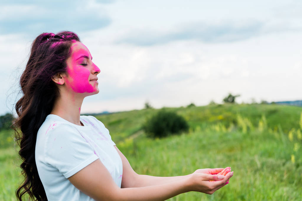 glückliche Frau mit pinkfarbener Holi-Farbe im Gesicht, stehend mit geschorenen Händen  - Foto, Bild