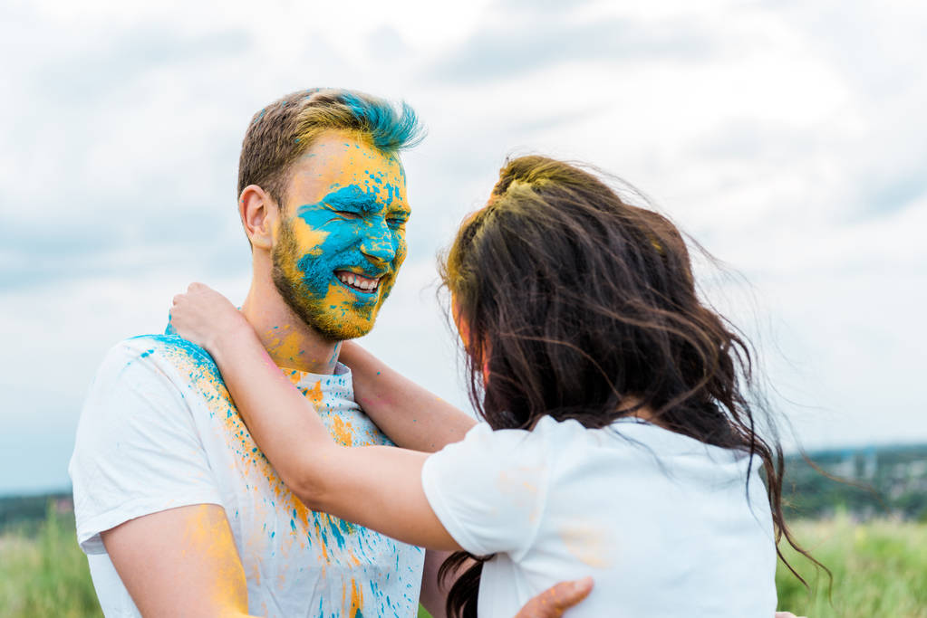 若い女性の近くの顔に目を閉じてホリ塗料を持つ幸せな男性の選択的な焦点  - 写真・画像