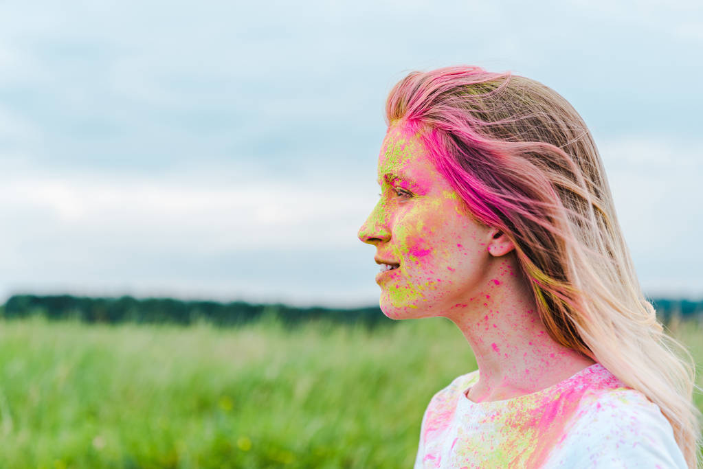 vista lateral de la joven feliz con pintura holi amarillo y rosa en la cara
  - Foto, imagen