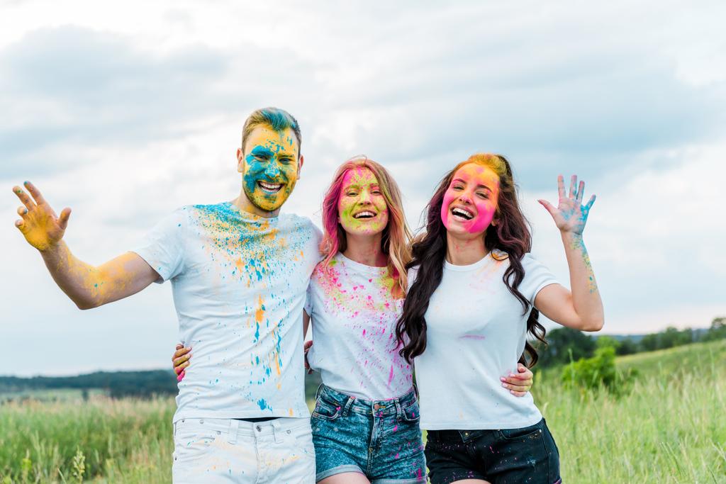 happy group of friends with holi paints on faces smiling outdoors  - Photo, Image