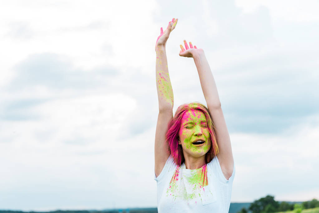 fiatal nő csukott szemmel, zöld és rózsaszín Holi festéket a kinyújtott kezet  - Fotó, kép