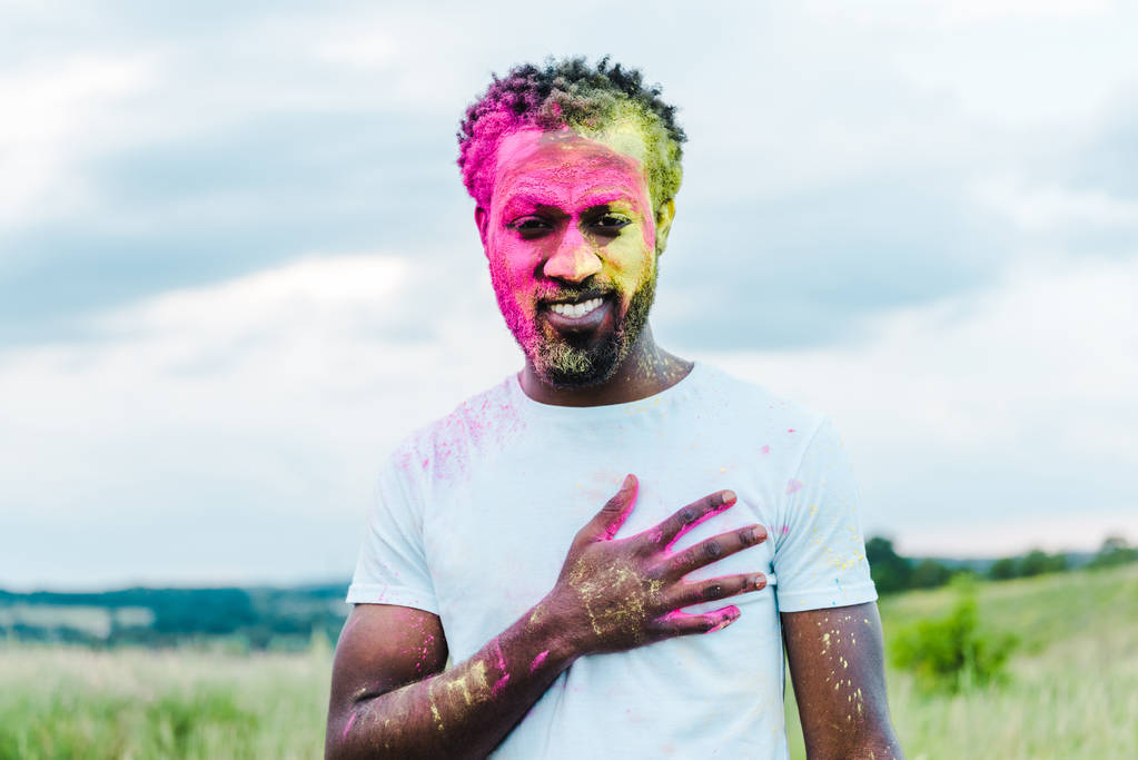 šťastný afroamerický muž v bílém tričku a barevném holi maluje na obličeji - Fotografie, Obrázek