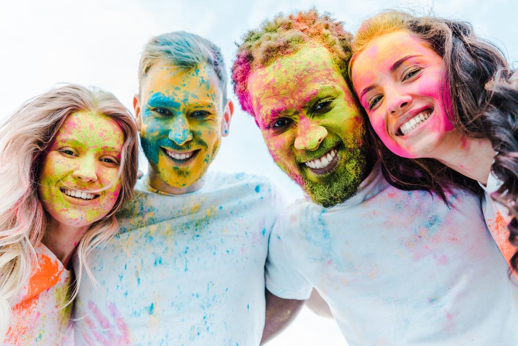 vista inferior de amigos multiculturais felizes com tintas holi coloridas em rostos
 - Foto, Imagem