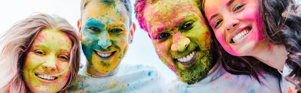 panoramic shot of happy multicultural friends with colorful holi paints on faces - Photo, Image