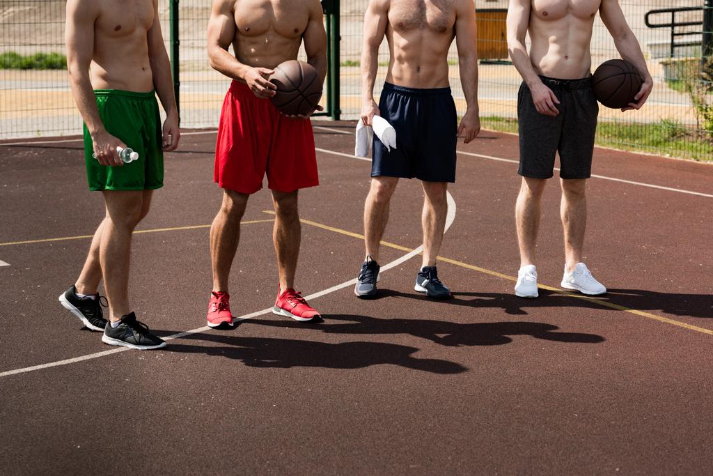Ausgeschnittene Ansicht von vier hemdlosen Basketballspielern mit Bällen auf dem Basketballplatz - Foto, Bild