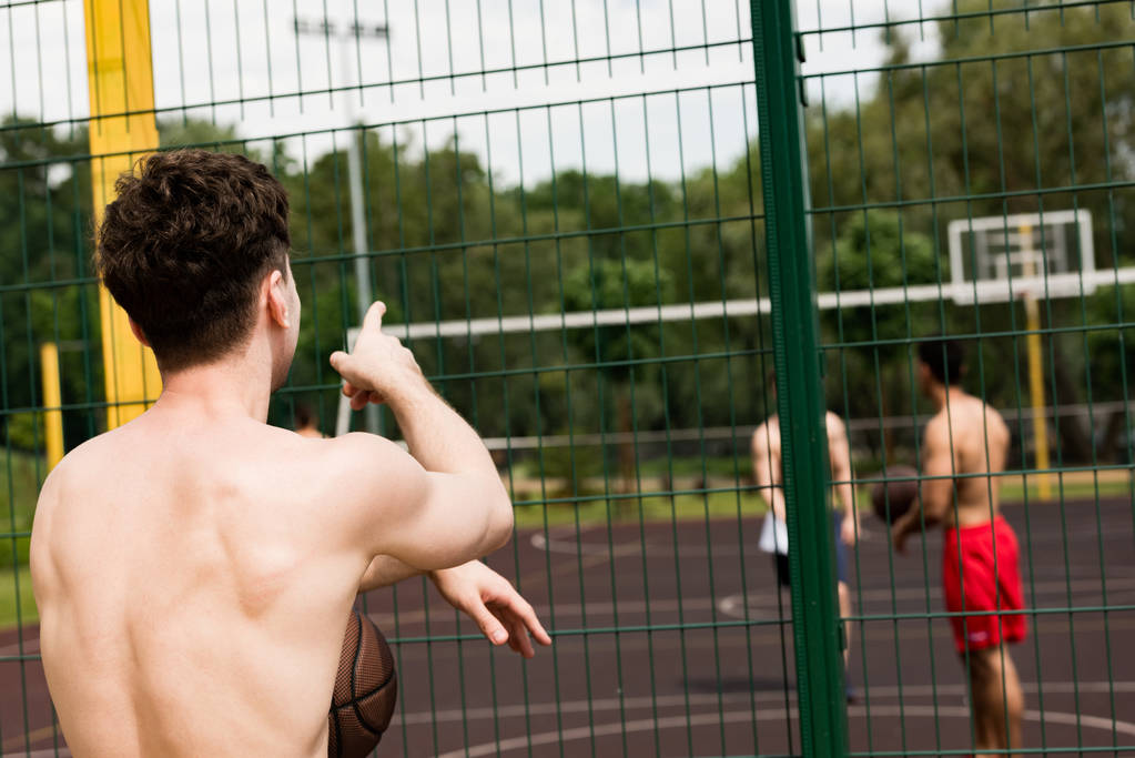 vue arrière du joueur de basket-ball torse nu avec balle regardant des amis et pointant du doigt le terrain de basket-ball
 - Photo, image