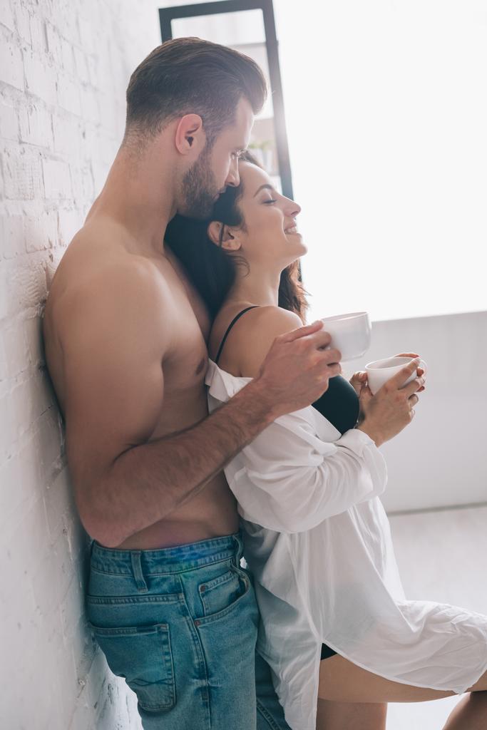 side view of handsome man and sexy woman holding cups near wall - Photo, Image