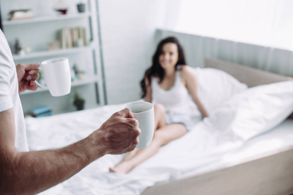 お茶とベッドに座っている女性とカップを保持する男性の選択的な焦点  - 写真・画像