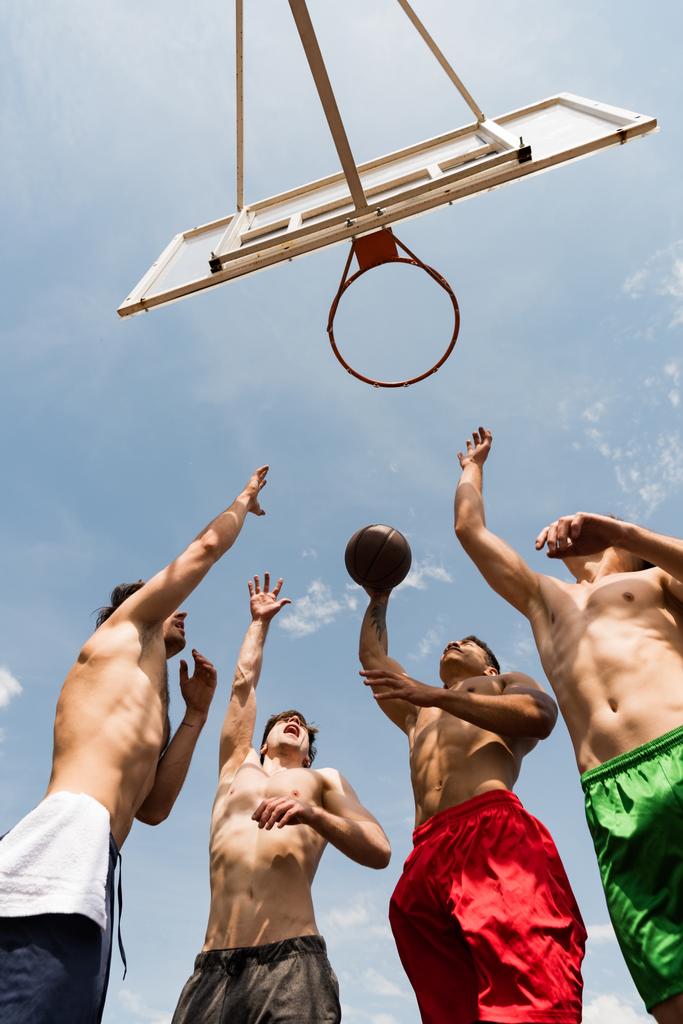 Bottom View van shirtless sporters spelen basketbal onder blauwe hemel - Foto, afbeelding